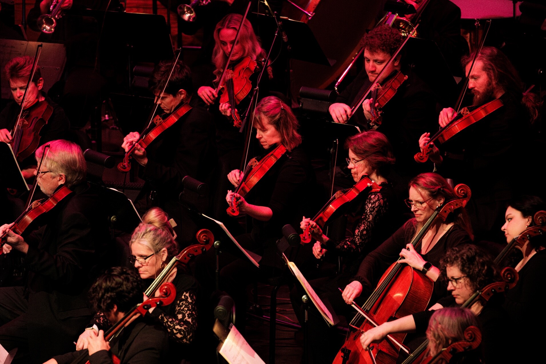 Boise Phil string musicians perform under red stage lighting.