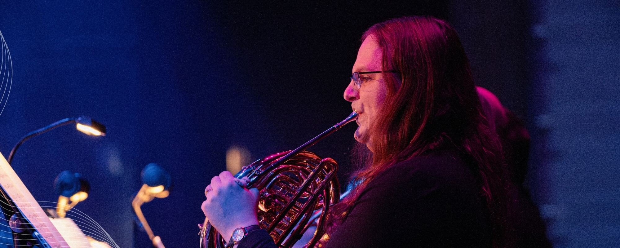 A Boise Phil French horn player performs under colorful stage lighting.
