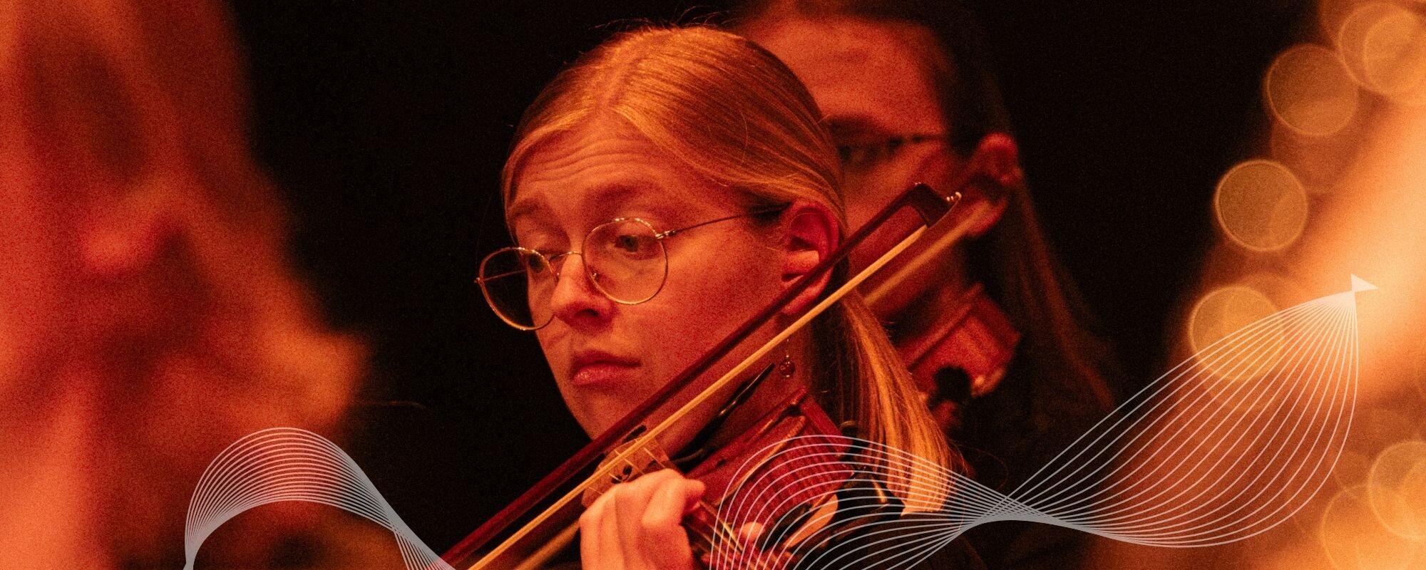 A Boise Phil violinist performs under warm orange stage lighting.